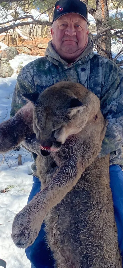 Hunter holding up a mountain lion in snowy woods