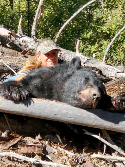 Hunter with a black bear draped over a log
