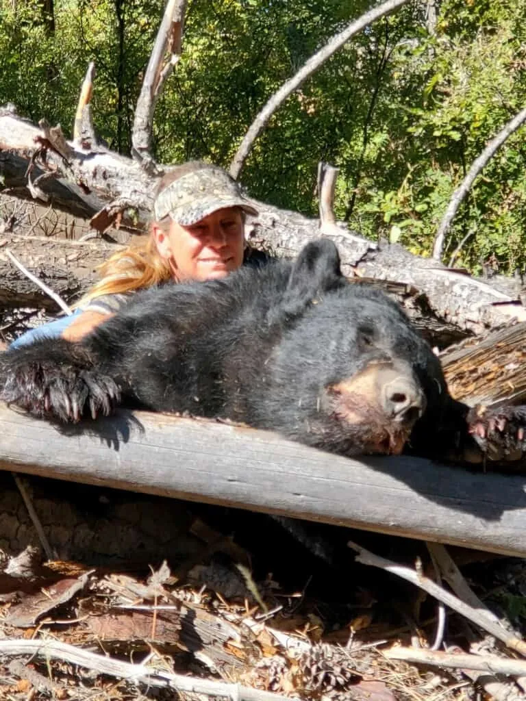 Hunter with a black bear draped over a log