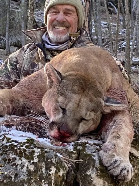 Smiling hunter with a mountain lion in the snow